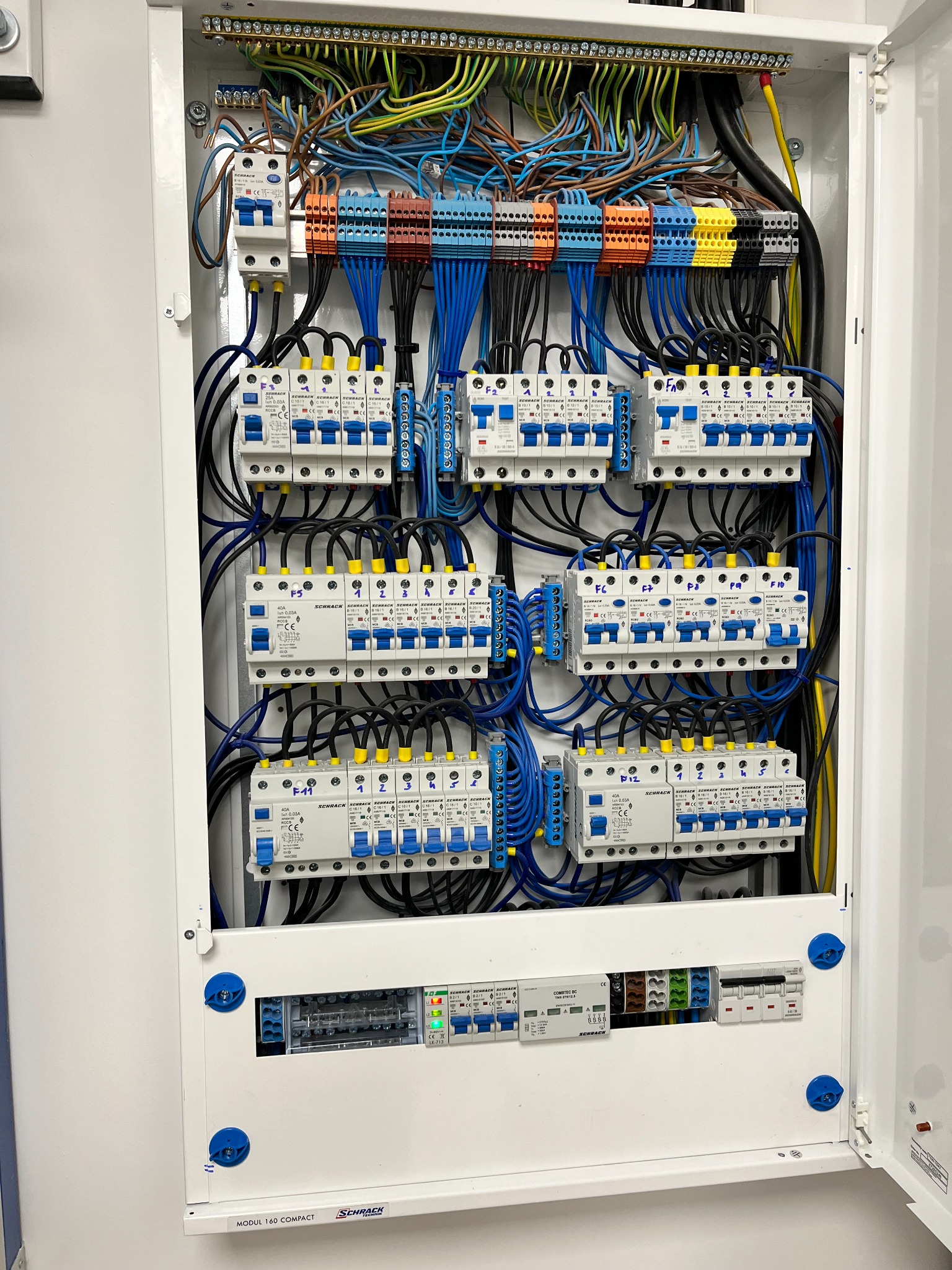 Rozdzielnica elektryczna Schrack z zainstalowanymi bezpiecznikami, przewodami o różnych kolorach i listwami zaciskowymi wewnątrz białej obudowy.