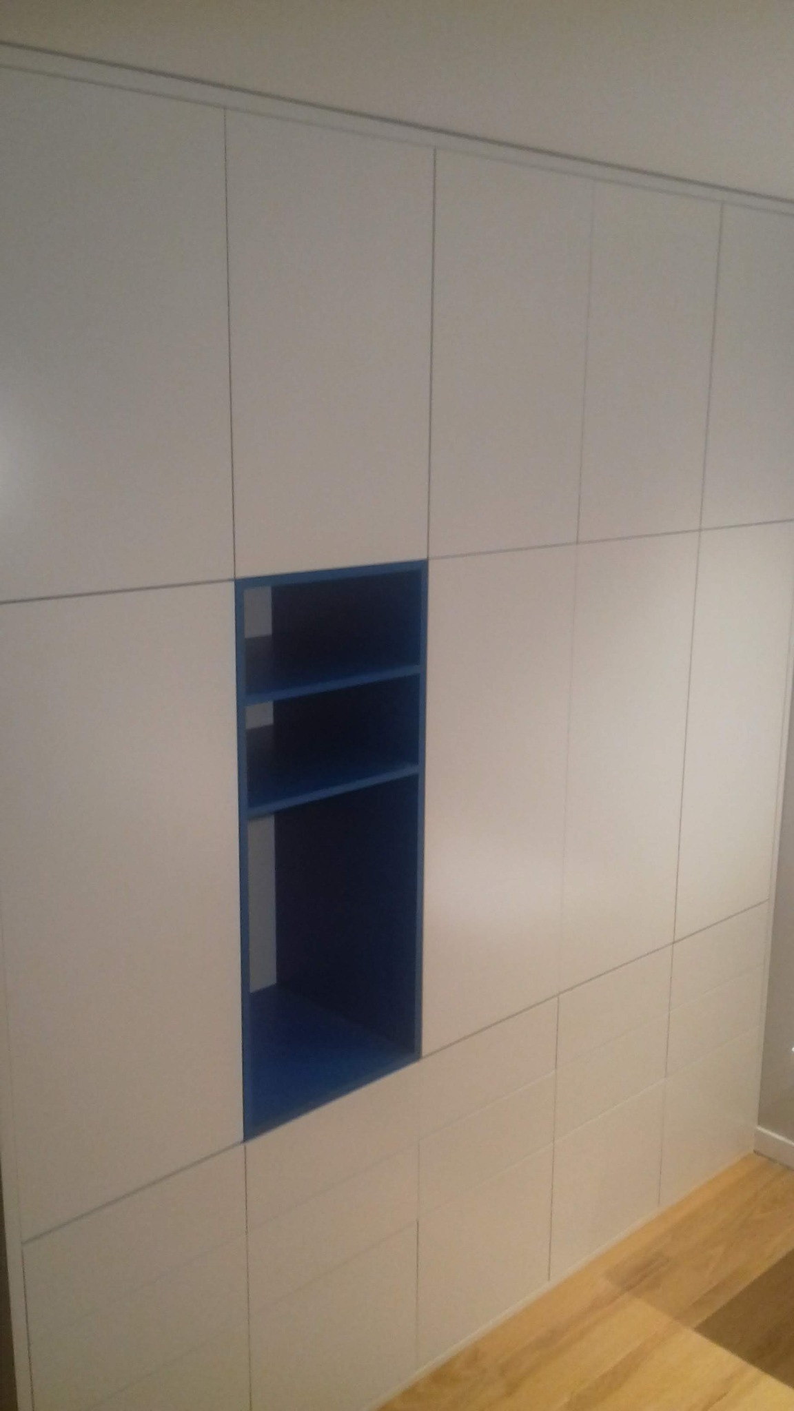 Biała szafa wnękowa z niebieską otwartą półką, widoczna podłoga z paneli.