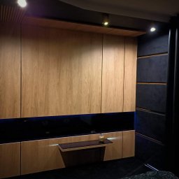 Zabudowa sypialni. Połączenie Hikory EGGER z czarnym szkłem lacobel, panele tapicerowane czarnym velurem wykończone aluminiowymi listwami w kolorze złota.