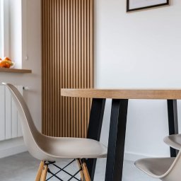 ARTezze - Stół z blatem drewnianym na czarnych nogach i krzesła w stylu skandynawskim, na tle dekoracyjnej drewnianej ściany z listew.