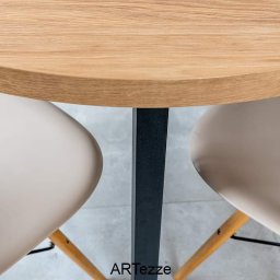 ARTezze - Okrągły blat drewniany z widoczną strukturą drewna, wsparty na czarnej, kwadratowej nodze, pomiędzy dwoma krzesłami z beżowymi siedziskami i drewnianymi nogami.