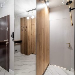 ARTezze - Nowoczesny przedpokój z lustrzaną szafą przesuwną, drewnianą zabudową z wieszakami widoczną w odbiciu, marmurową podłogą i designerskim oświetleniem.