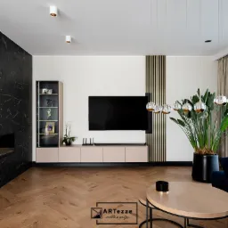 Salon z drewnianą podłogą w jodełkę, zabudową meblową w odcieniach beżu i czerni, przeszkloną witryną, dekoracyjną ścianą z czarnego marmuru i złotymi akcentami.