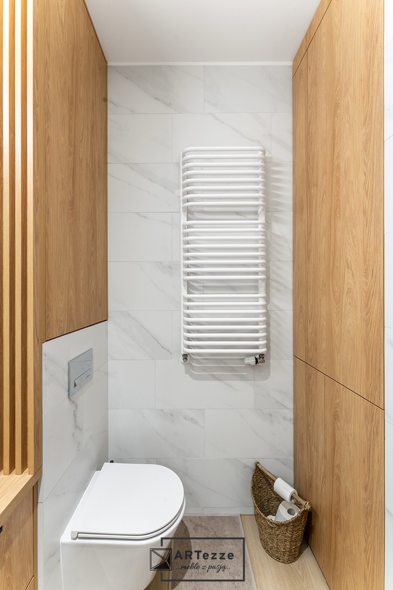 Nowoczesna łazienka z drewnianymi szafkami na wymiar, marmurowymi płytkami i białym grzejnikiem drabinkowym.