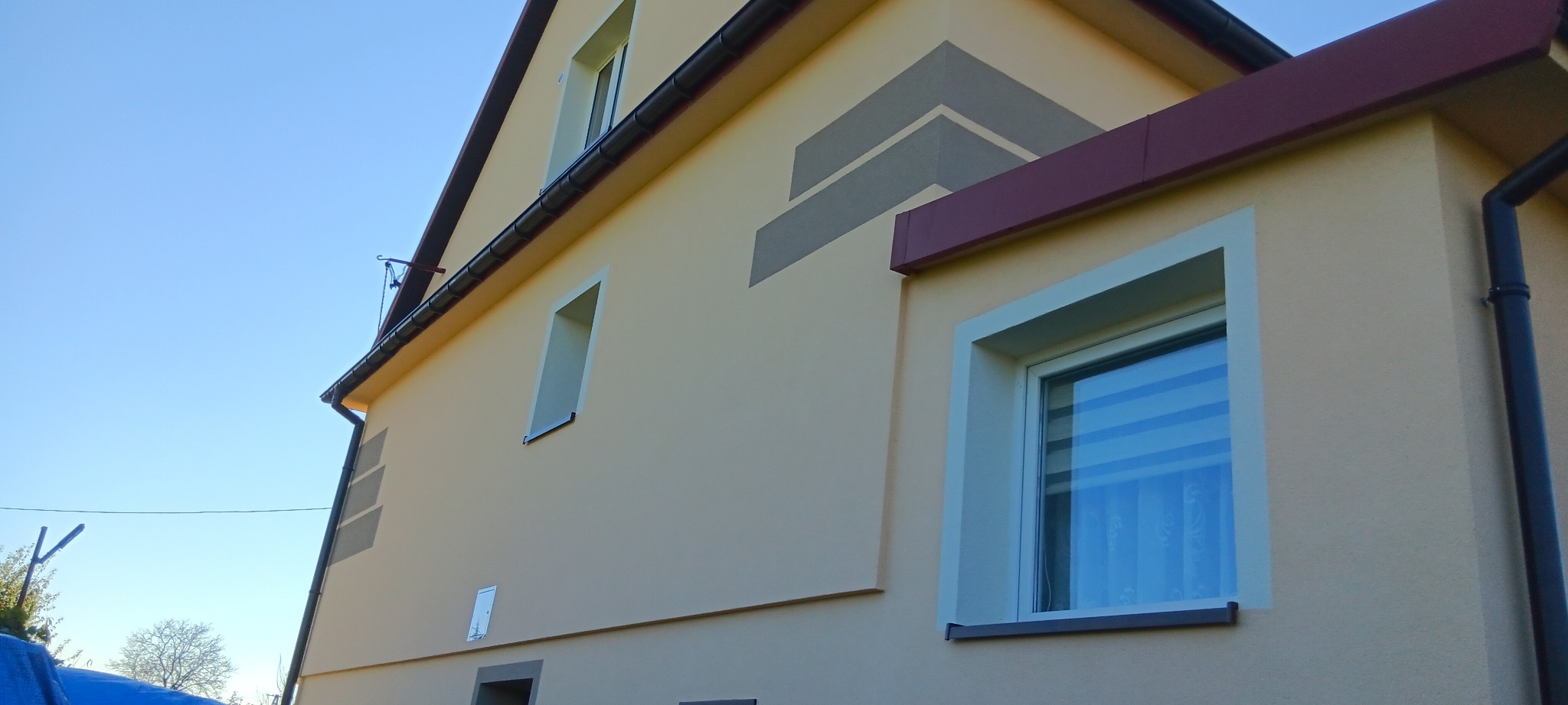 Jasna elewacja domu jednorodzinnego w Siemiechowie z dekoracyjnymi szarymi pasami i nowymi oknami, widok z dołu w słoneczny dzień.