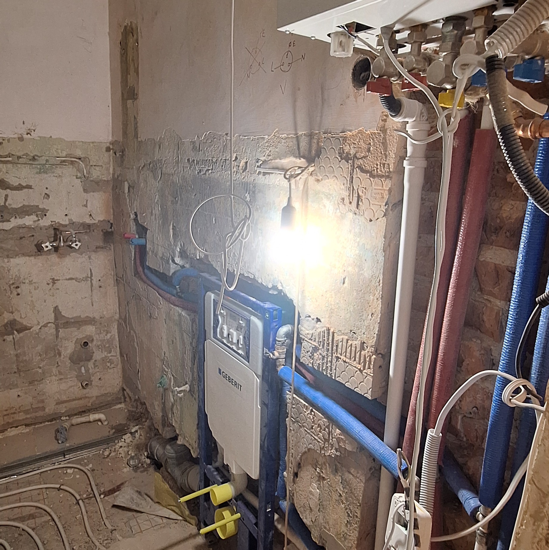 Montaż podtynkowego stelaża Geberit w łazience w trakcie remontu. Widoczne rury, instalacja wodna i ściany w stanie surowym z elementami starej glazury.