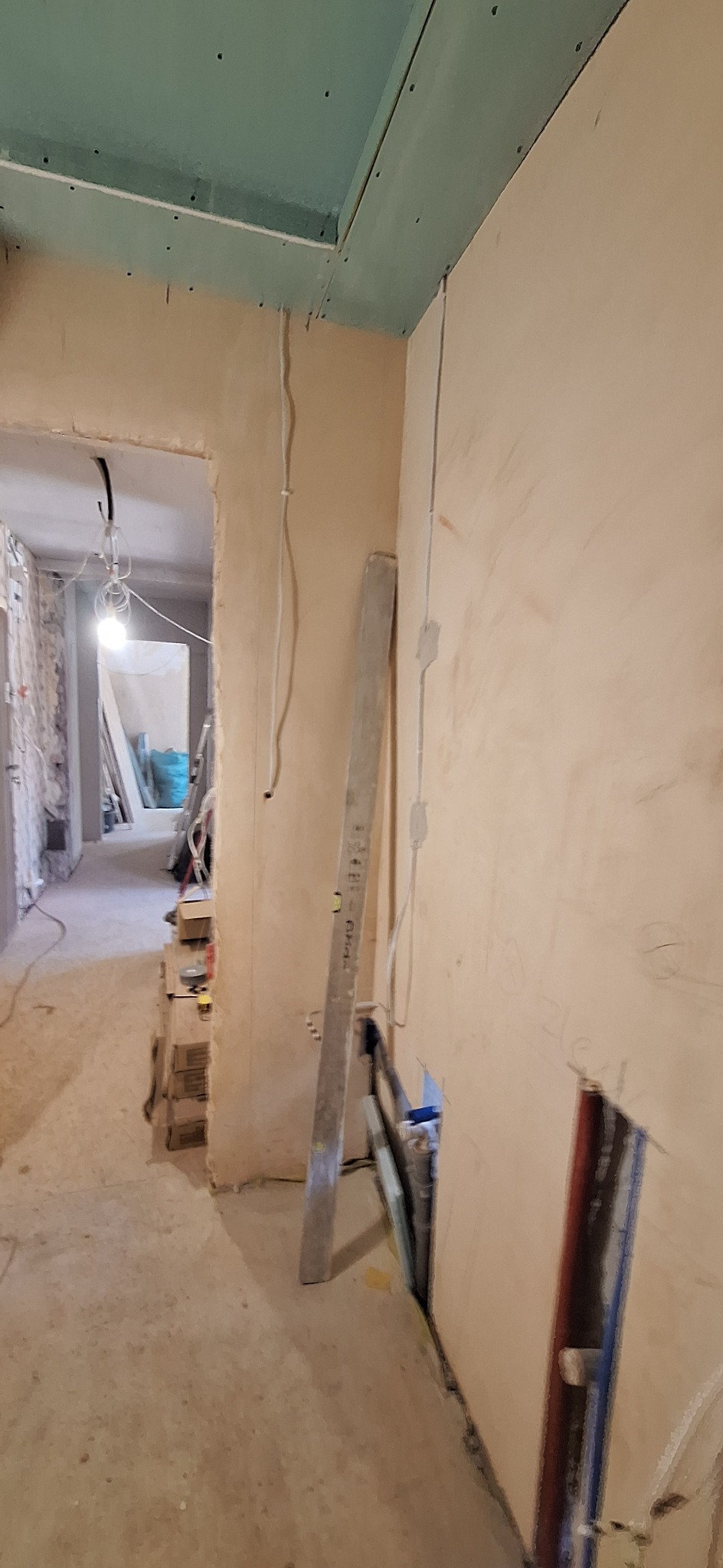 Wnętrze w trakcie remontu: ściany z nałożonym tynkiem, widoczne przewody elektryczne, zamontowana płyta gipsowa na suficie, poziomica oparta o ścianę, narzędzia.