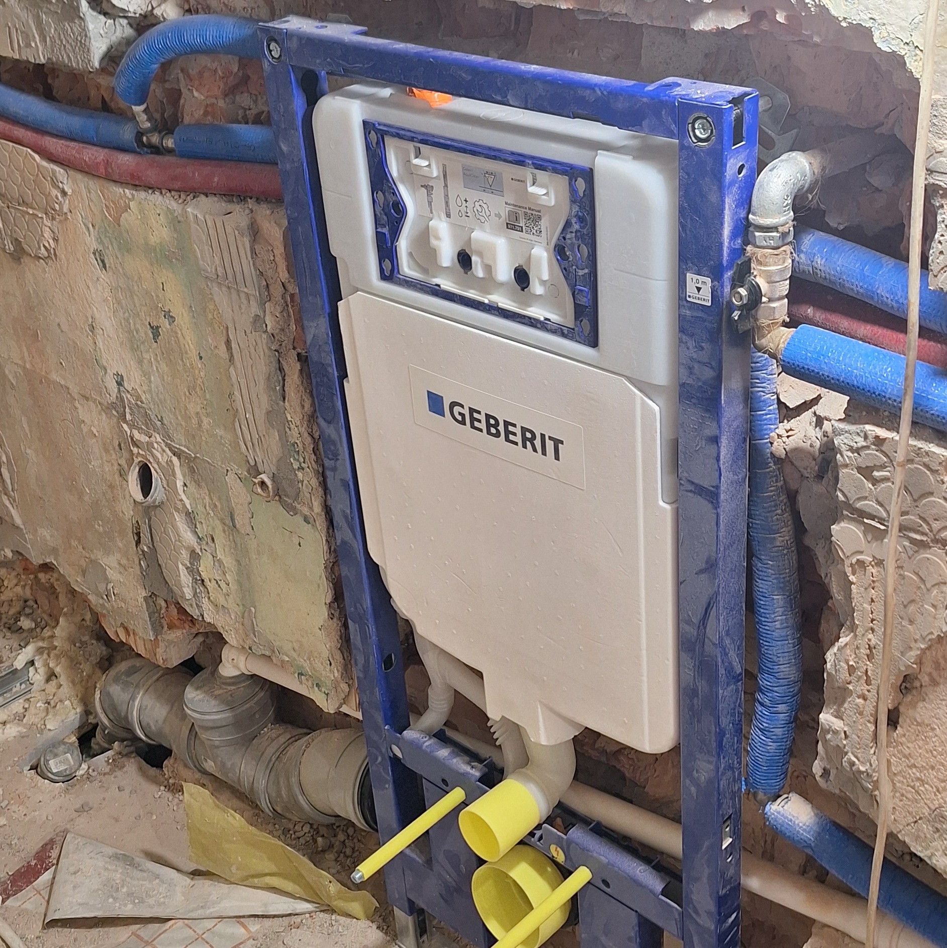 Stelaż podtynkowy Geberit zamontowany w surowej łazience z widocznymi instalacjami wodnymi i kanalizacyjnymi. Etap prac przed wykończeniem.