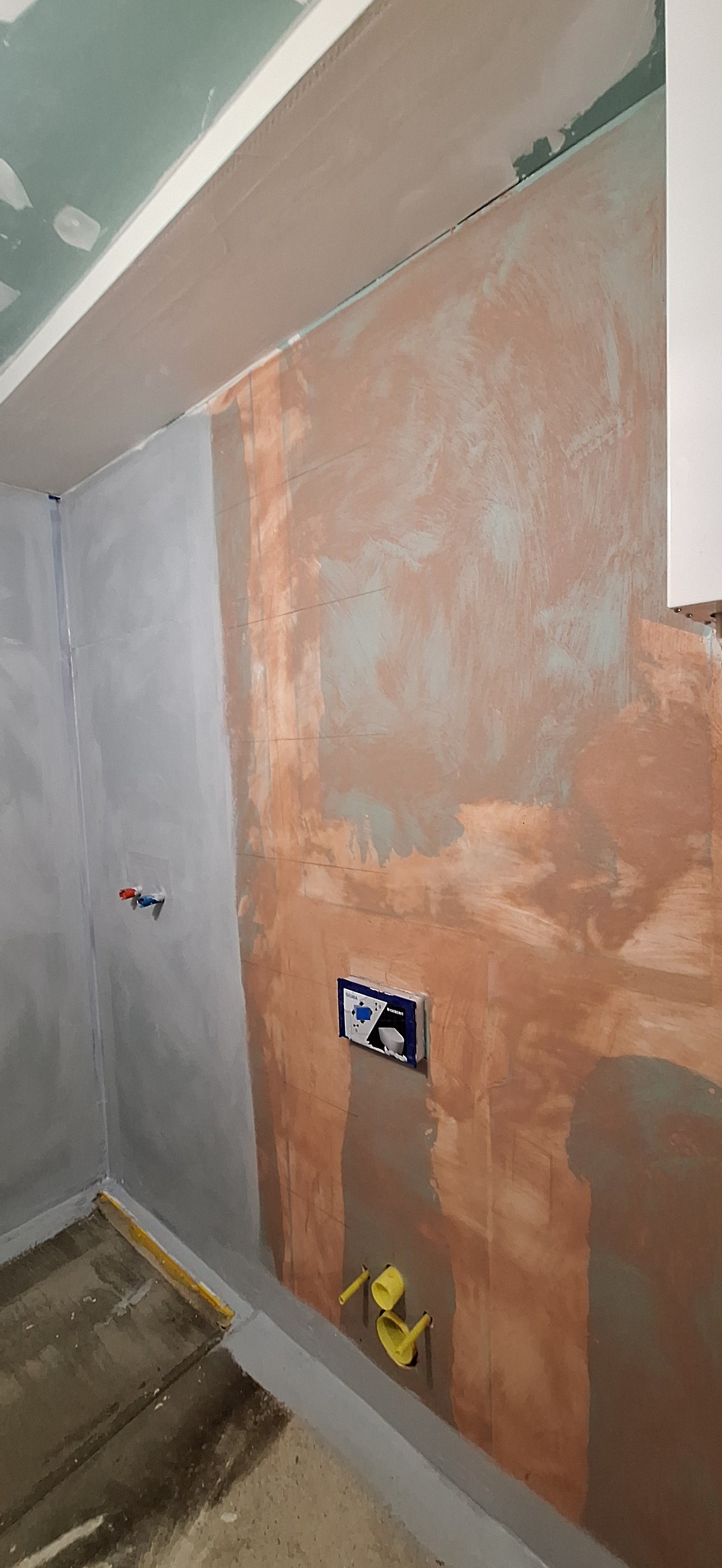 Ściana w łazience w trakcie przygotowywania podłoża pod płytki, widoczne pionowe linie i zamontowana podtynkowa instalacja WC.