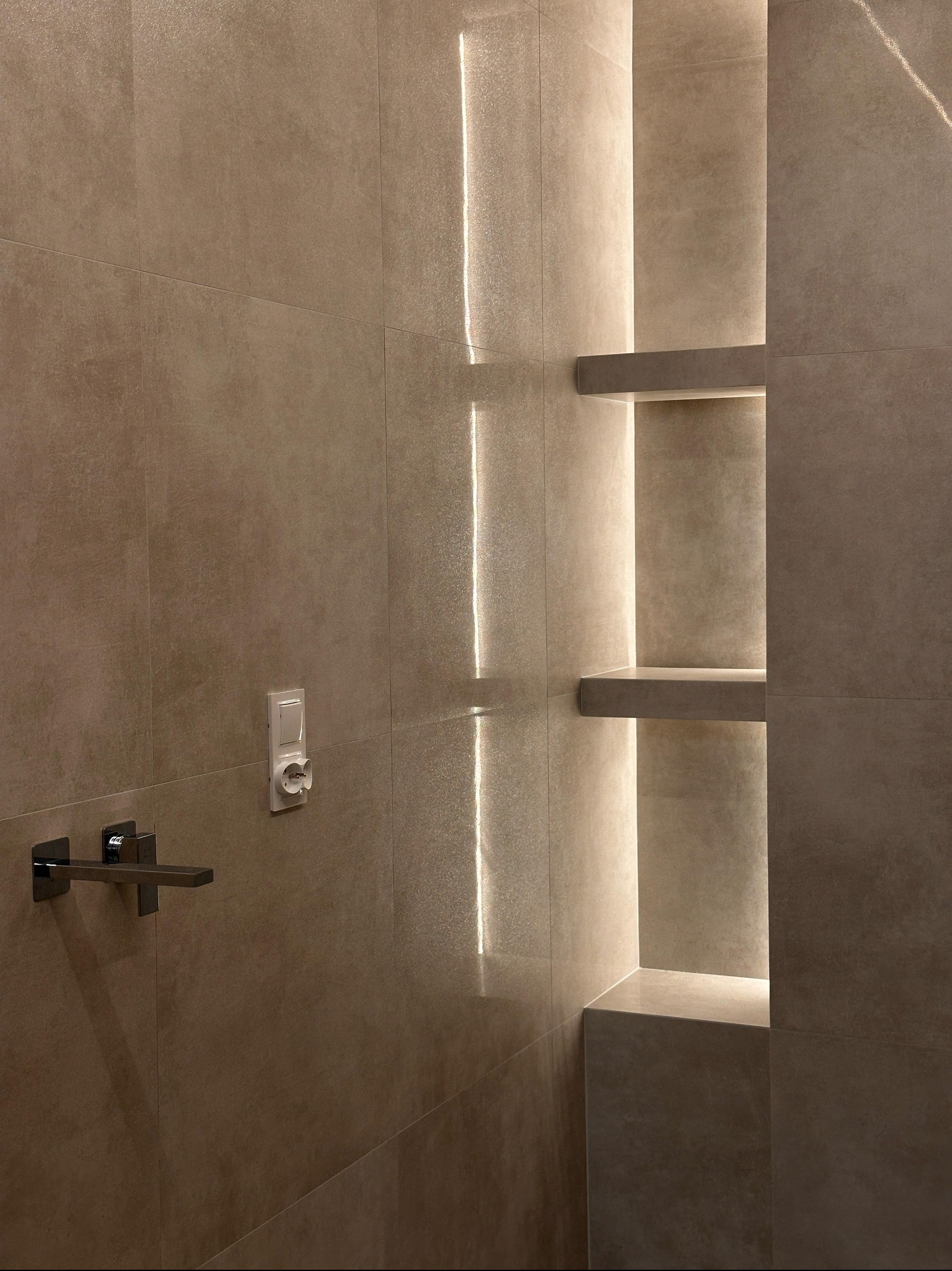 Beżowa łazienka z podświetlanymi półkami wnękowymi, minimalistyczna bateria umywalkowa i kontakt. Nowoczesny design, ciepłe oświetlenie.