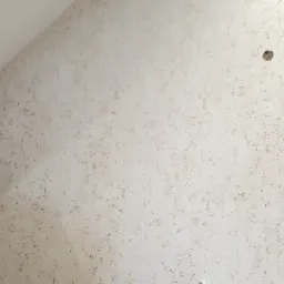 Ściana w beżowej tapecie z delikatnym wzorem, widoczny fragment schodów z drewnianą barierką oraz fragment salonu z szafką RTV i telewizorem.