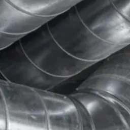 Metalowe, spiralnie zwijane rury wentylacyjne, połączone ze sobą, widoczne z bliskiej perspektywy pod kątem, z delikatnymi refleksami światła.