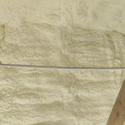 Jasna, nierówna powierzchnia pokryta pianką izolacyjną, widoczny fragment drewnianej konstrukcji dachu i kabel.