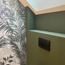 Royal Finish Piotr Piórkowski - Wykończona łazienka: ściana z motywem roślinnym, zielona ściana z czarnym przyciskiem spłuczki, biały sufit. Nowoczesny design z akcentem natury.