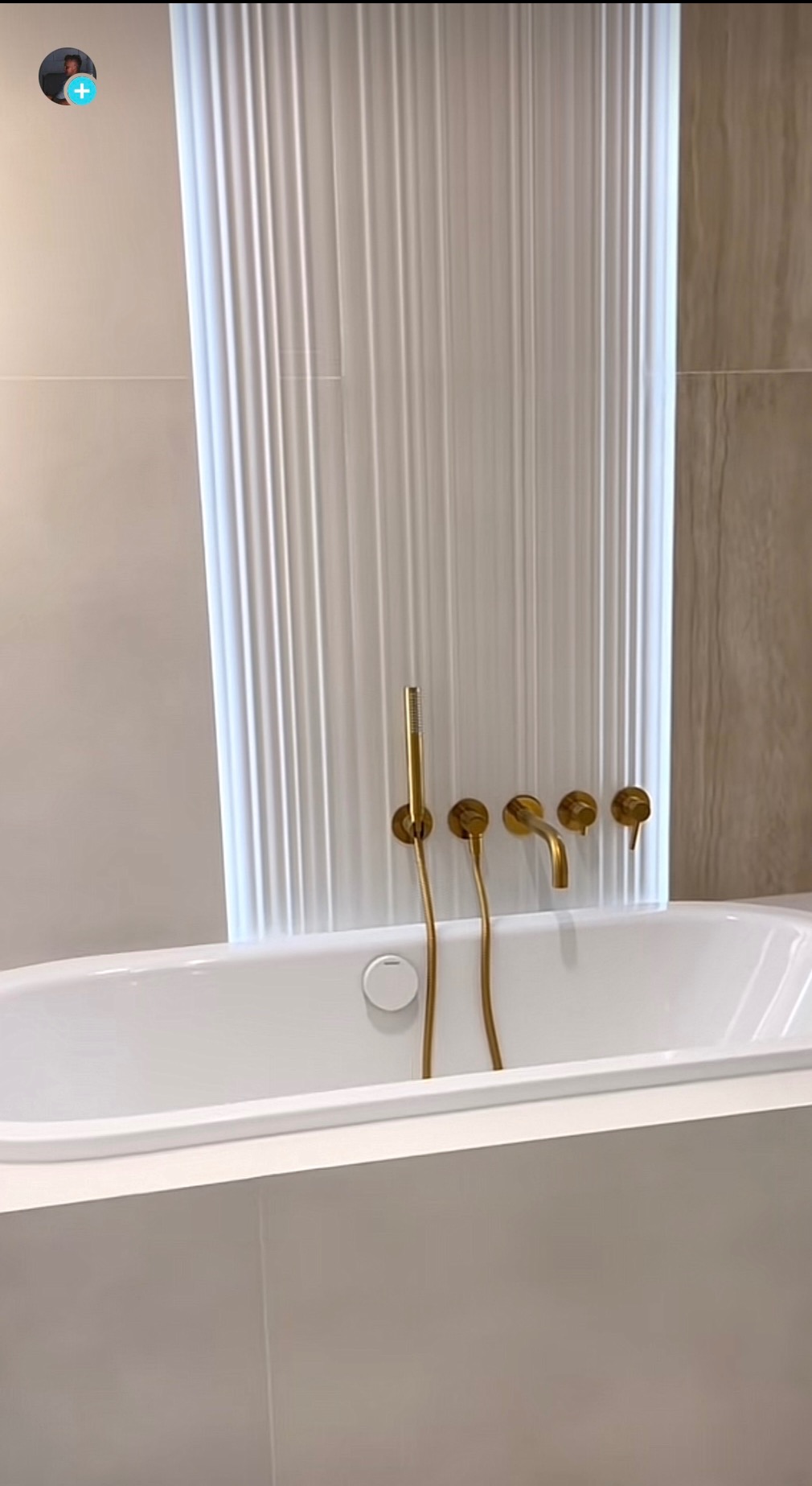 Biała wanna z baterią w kolorze złotym i dekoracyjnym panelem ściennym z pionowymi żłobieniami.