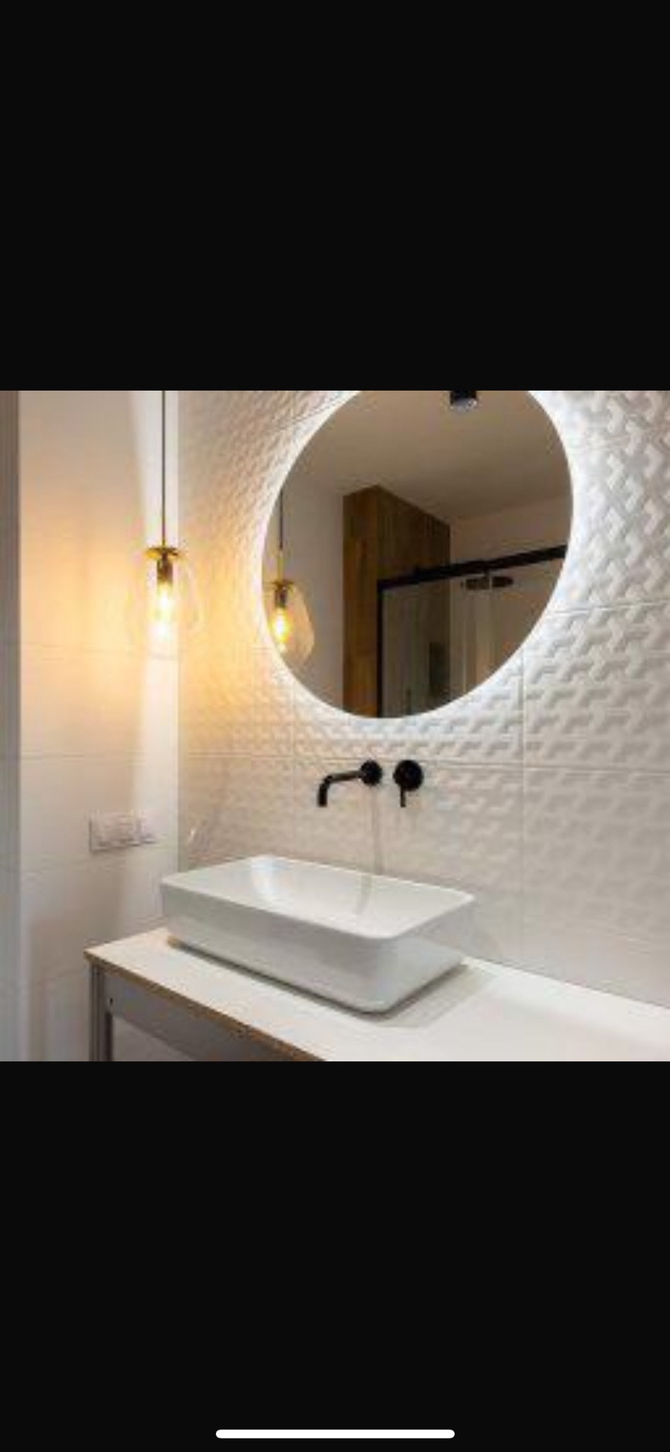 Nowoczesna łazienka z umywalką nablatową, czarną armaturą i okrągłym lustrem z podświetleniem LED, na ścianie białe płytki 3D, widoczne wiszące lampy z żarówkami Edison