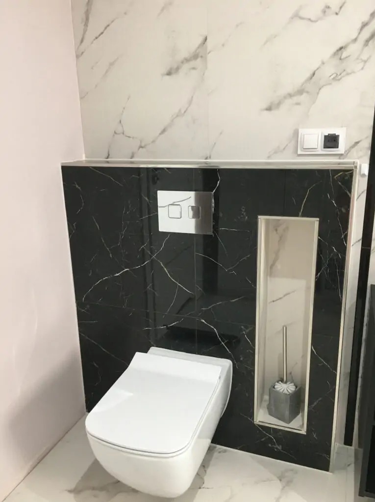 Nowoczesna łazienka z podwieszaną toaletą, czarnym marmurem na ścianie i wnęką na szczotkę toaletową.