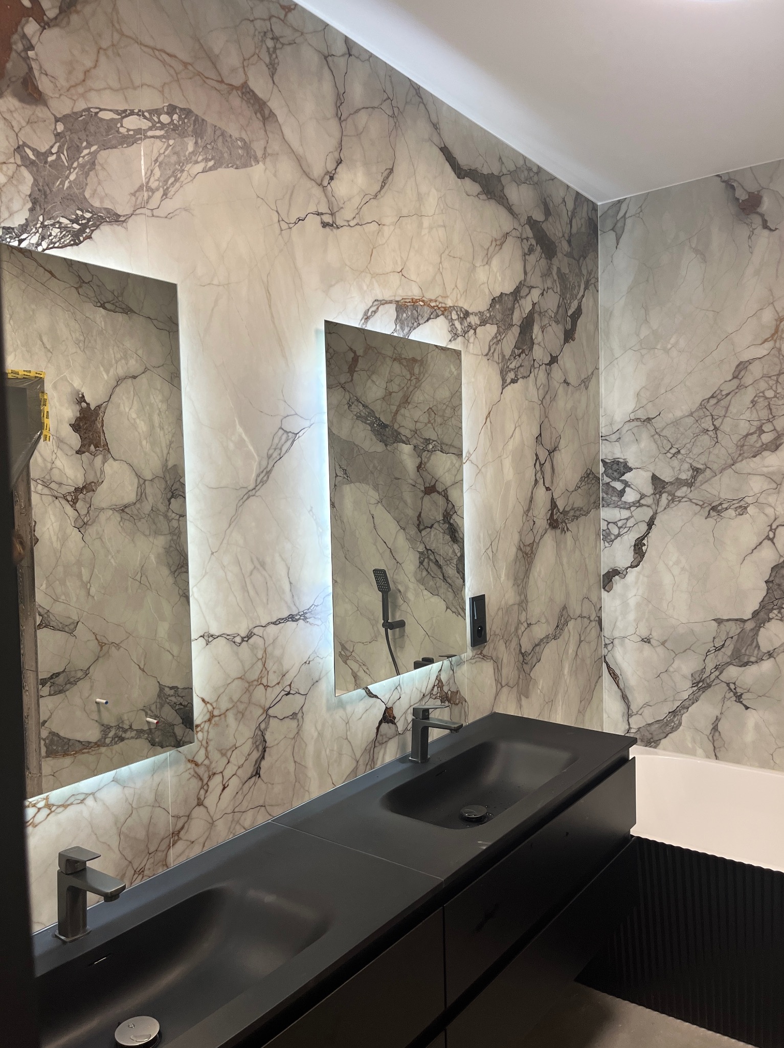 Elegancka łazienka z dwoma umywalkami w kolorze antracytu, marmurowymi płytami na ścianach i podświetlanymi lustrami. Nowoczesny design.