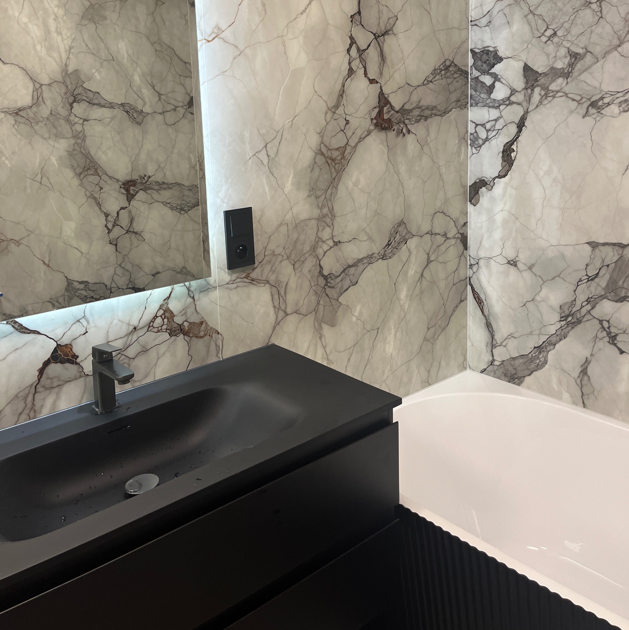 Nowoczesna łazienka z czarną umywalką nablatową i marmurowymi płytkami na ścianach. Minimalistyczny design, eleganckie wykończenie.