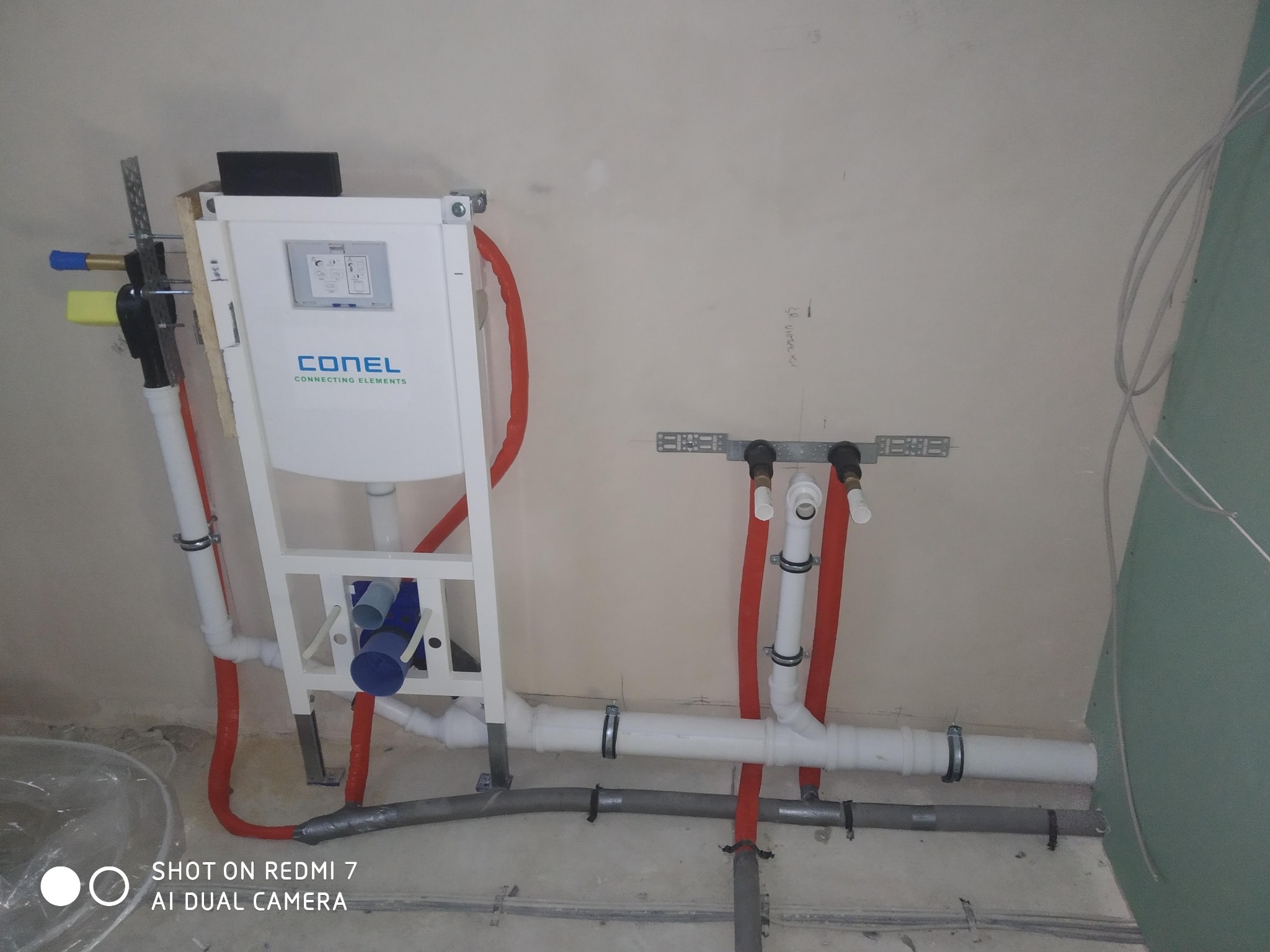 Stelaż podtynkowy WC marki Conel z podłączonymi rurami doprowadzającymi wodę, widoczne elementy instalacji hydraulicznej przed zabudową, ściany w stanie surowym.