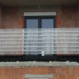 Nowa, aluminiowa balustrada balkonowa z poziomymi profilami, jeszcze w folii ochronnej, zamontowana na balkonie w surowym stanie, widoczna czarna izolacja przeciwwilgociowa.