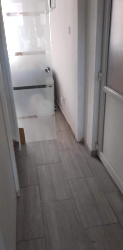 Wykończona łazienka z szarymi płytkami podłogowymi ułożonymi wzdłuż korytarza, widoczne dwie pary drzwi w bieli.