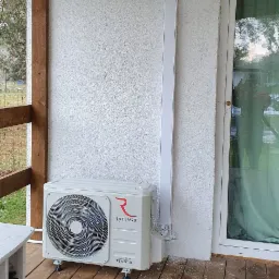 Zewnętrzna jednostka klimatyzacji Rotenso Inverter zamontowana na drewnianym tarasie przy ścianie budynku z widoczną listwą maskującą przewody.