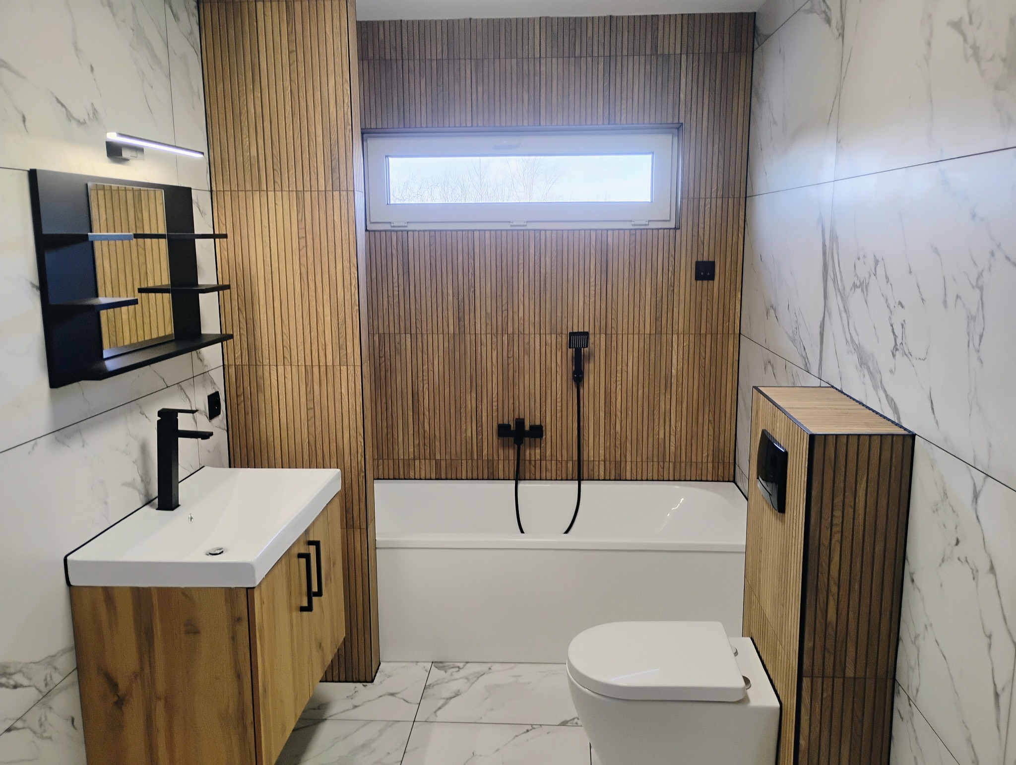 Nowoczesna łazienka z marmurowymi płytkami i drewnianymi lamelami, czarna armatura, biała ceramika, okno z widokiem na drzewa. Minimalistyczny design.