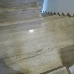 Jasne, kamienne schody wewnętrzne z podświetleniem stopnia i dekoracyjnym wykończeniem ściany w kształcie zębów piły.