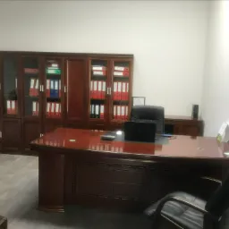 Biuro z ciemnego drewna z regałami wypełnionymi segregatorami, laptop i kalkulator na blacie, czarne krzesło biurowe