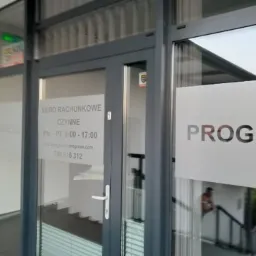 Wejście do biura rachunkowego z szarymi ramami okiennymi i szklanymi drzwiami, na których widnieje nazwa 'PROGRESS' oraz informacje o godzinach otwarcia i numerze telefonu.