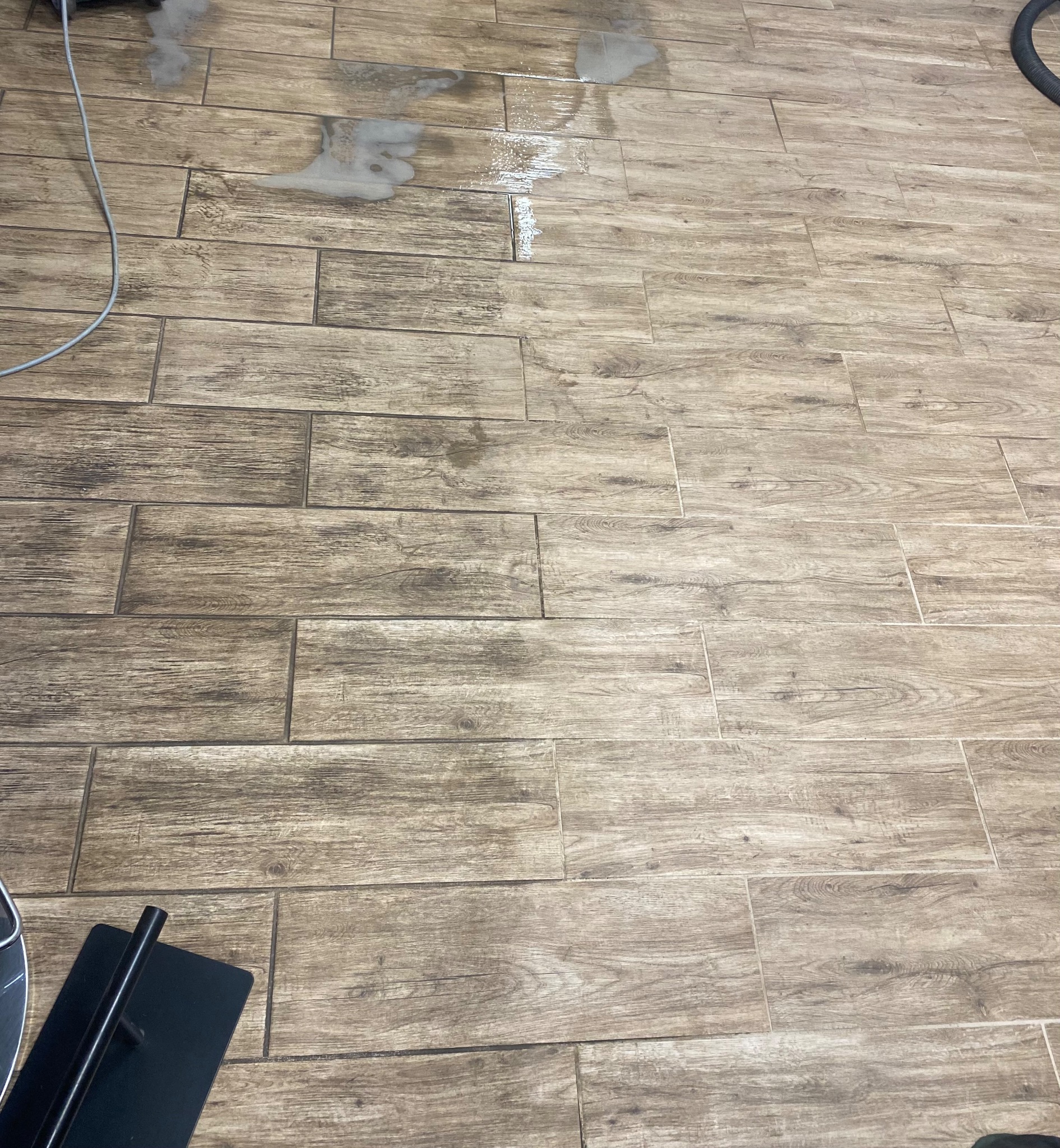 Czyszczenie podłogi z płytek imitujących drewno, widoczne ślady mokrej piany i urządzenie czyszczące.