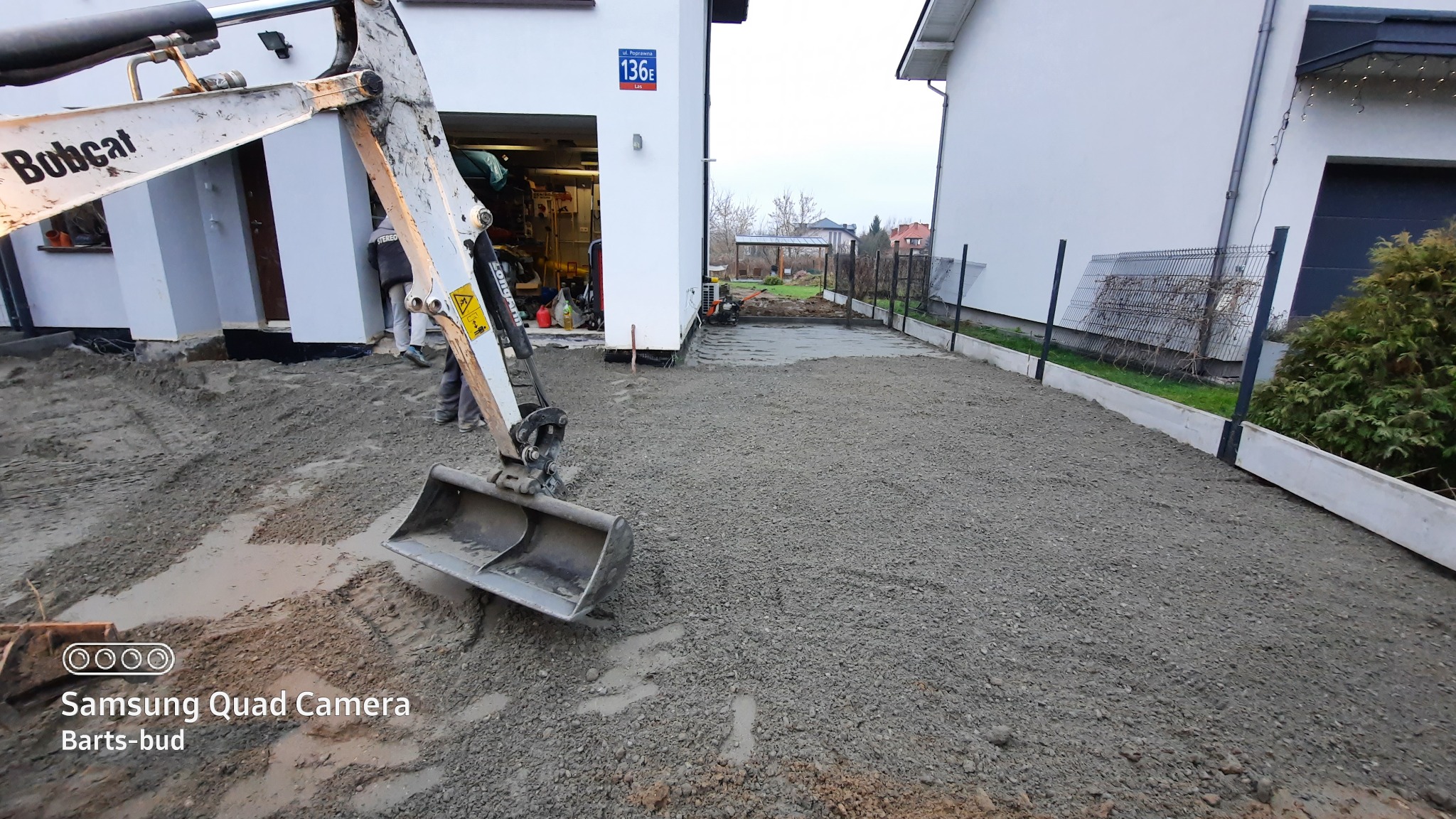 Przygotowanie podłoża pod kostkę brukową lub wylewkę betonową z użyciem mini koparki Bobcat, widoczne obrzeża betonowe i fragment ogrodzenia panelowego.