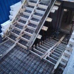 Zbrojenie schodów z deskowaniem i częściowo wymurowanymi ścianami z bloczków betonowych w surowym stanie.