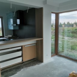 Firma Handlowo Usługowa Maciej Kaliszewski - Nowoczesna kuchnia w trakcie wykończenia: widoczne niezabezpieczone elementy, surowe ściany i podłoga betonowa, okna panoramiczne z widokiem na zieleń.