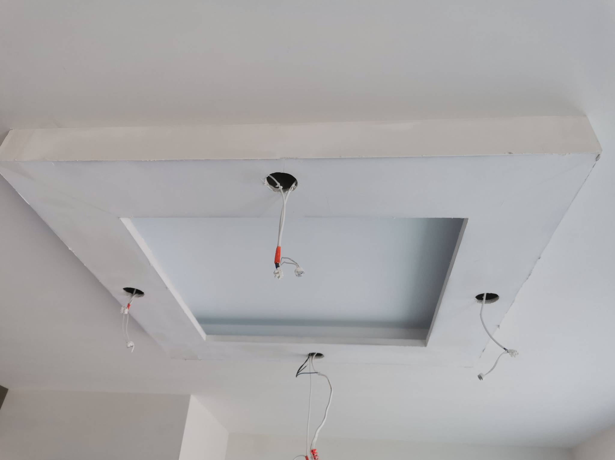 Biały sufit podwieszany z otworem na oświetlenie, widoczne przewody elektryczne.