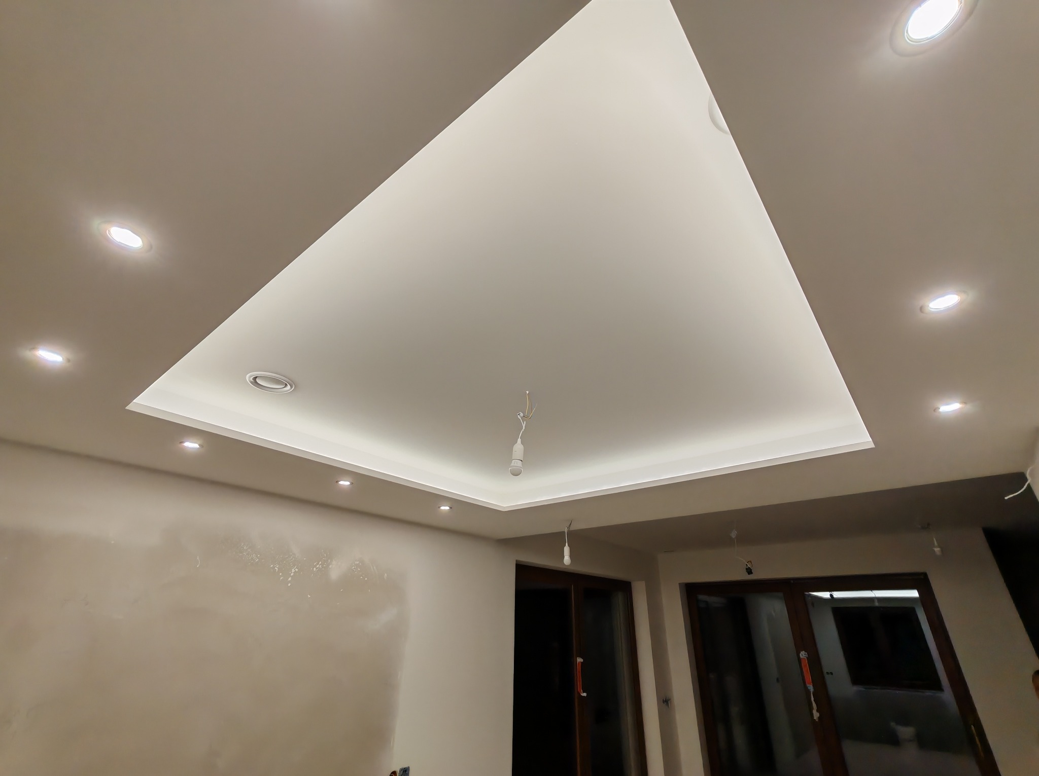 Nowoczesny sufit podwieszany z oświetleniem punktowym i centralnym, widoczne niedokończone ściany wymagające gładziowania.