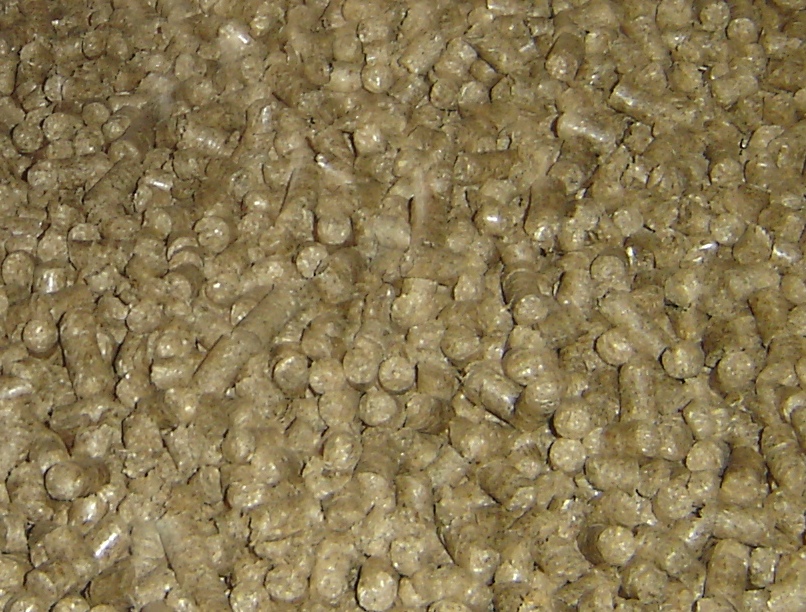 Jasnobrązowe granulki paliwa z biomasy, prawdopodobnie ze słomy lub łusek słonecznika, ułożone gęsto na płaskiej powierzchni, widoczne z bliska.