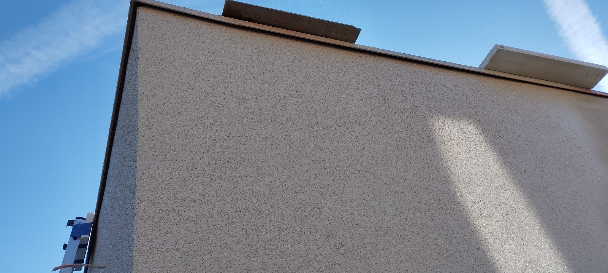 Elewacja budynku z fakturą baranka, widoczna drabina i fragment błękitnego nieba z smugą kondensacyjną.