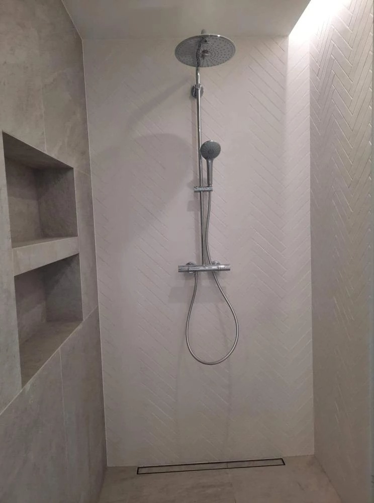 Nowoczesny prysznic z deszczownicą i wnęką w ścianie, wykończony płytkami w jodełkę.