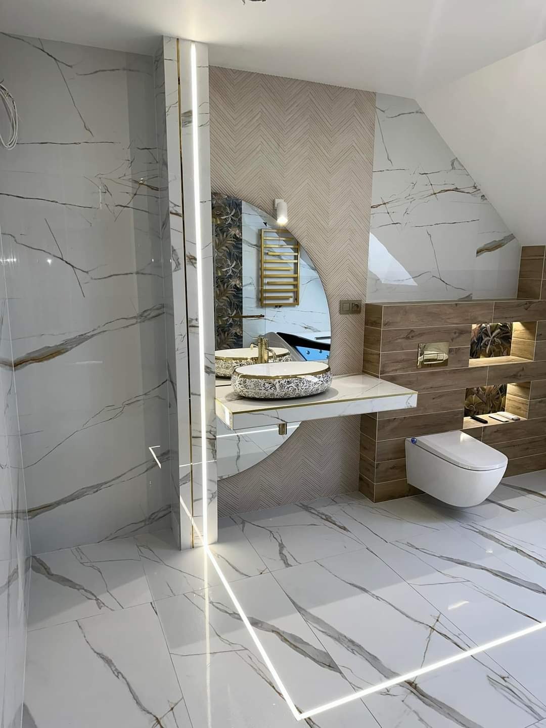 Nowoczesna łazienka z białymi marmurkowymi płytkami, owalnym lustrem i umywalką w stylu glamour z elementami złota, podświetlana listwa LED na podłodze.