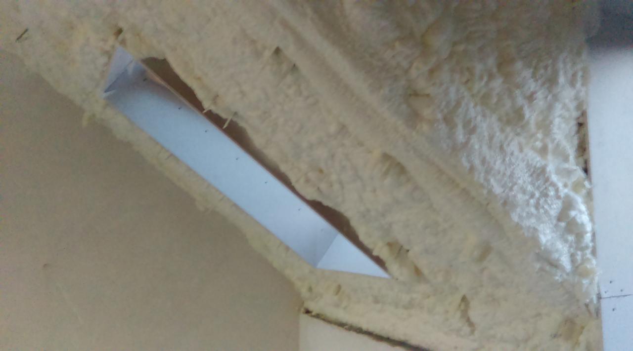 Poddasze z widoczną konstrukcją i zaaplikowaną pianką izolacyjną, tworzącą nierówną powierzchnię wokół otworu.