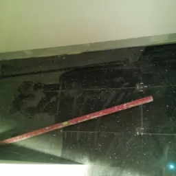 Ciemne, błyszczące płytki ścienne z poziomnicą i listwą, w trakcie układania, widoczne ślady kleju i linie pomocnicze.