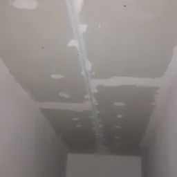 Niedokończony sufit z widocznymi łatami gipsowymi i listwą montażową, przygotowany do dalszych prac wykończeniowych.