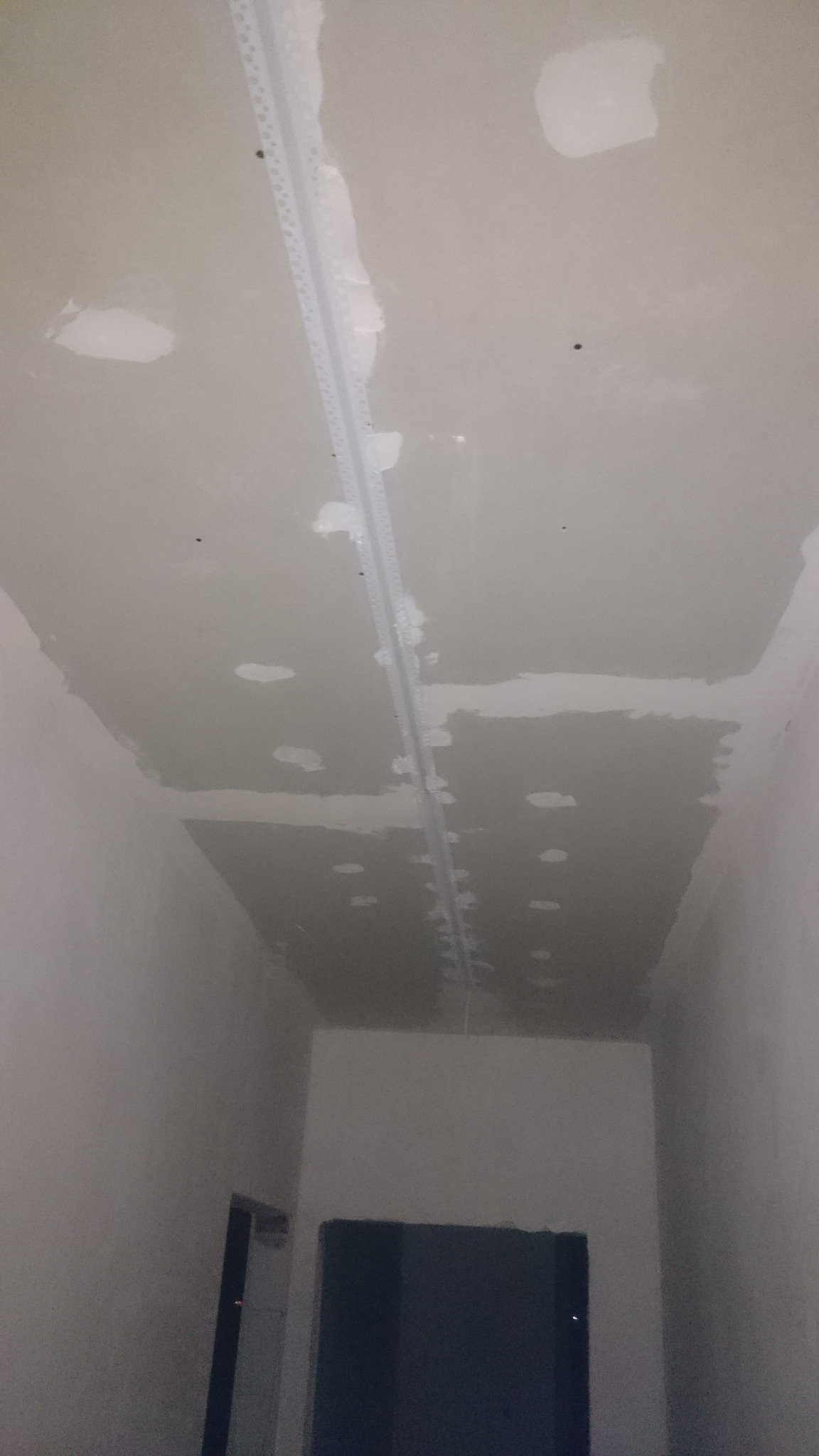 Niedokończony sufit z widocznymi łatami gipsowymi i listwą montażową, przygotowany do dalszych prac wykończeniowych.