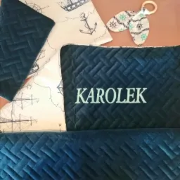 Komplet wyprawki niemowlęcej z granatowego pikowanego weluru z imieniem 'Karolek', pościel w marynistyczne wzory (statki, kotwice) oraz gryzak z tkaniny w sterowe koła.