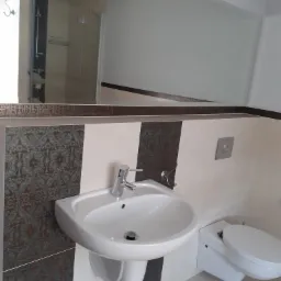 Nowoczesna łazienka z umywalką nablatową, toaletą podwieszaną i dużym lustrem, wykończona płytkami w geometryczne wzory i odcieniach bieli oraz szarości.