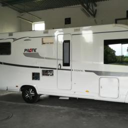 Auto-Komplex Michał Zielonka - Biały kamper marki Pilote Essentiel G740 w warsztacie, widoczne otwarte drzwiczki serwisowe i stolik roboczy z narzędziami.