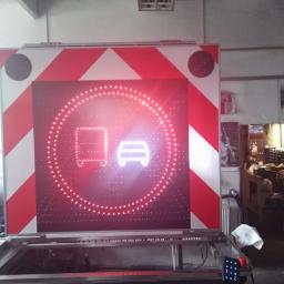 Auto-Komplex Michał Zielonka - Duży znak drogowy LED z czerwonymi i białymi pasami ostrzegawczymi, wyświetlający ikonę samochodu osobowego i ciężarowego w czerwonym okręgu, prawdopodobnie zakaz wjazdu, w warsztacie.