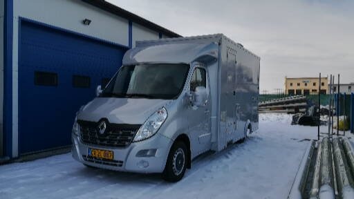 Srebrny samochód dostawczy Renault Master z zabudową kontenerową zaparkowany na śniegu przed niebieską bramą garażową.